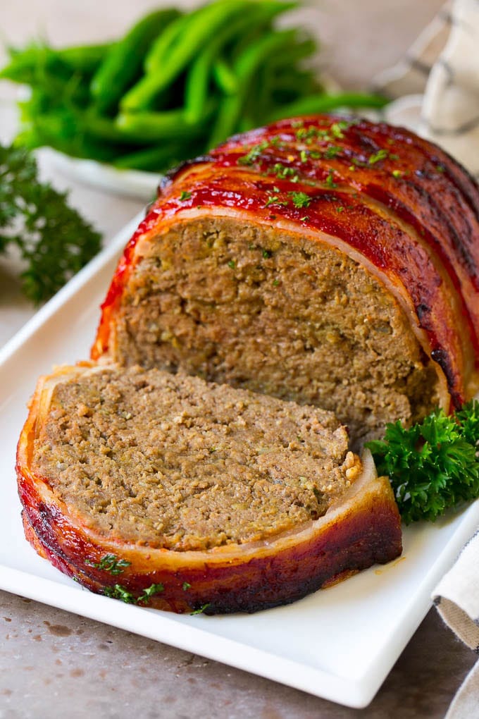 Bacon Wrapped Meatloaf Recipe | Beef Meatloaf #meatloaf #beef #groundbeef #bacon #dinner #sraye A bacon wrapped meatloaf with a slice out of it, on a serving platter.