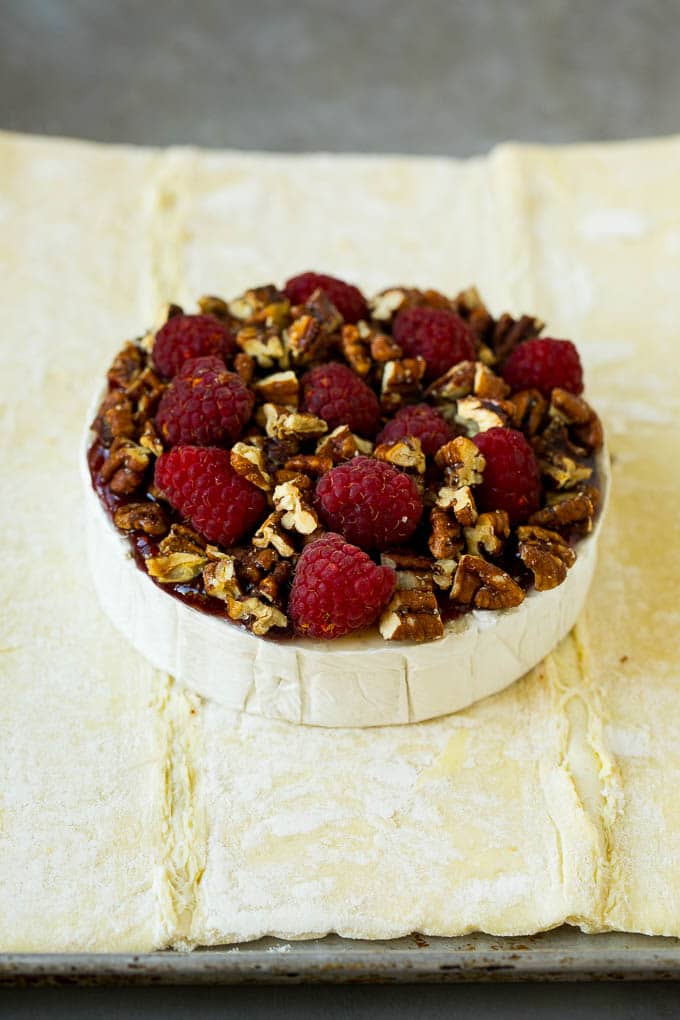 Baked Brie Recipe | Pastry Wrapped Brie #brie #cheese #appetizer #pecans #raspberries #sraye A wheel of cheese topped with jam, raspberries and pecans.