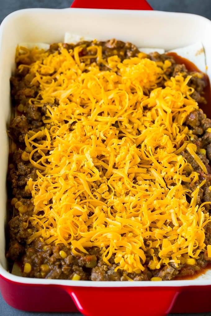 Mexican Lasagna Recipe | Mexican Casserole #mexican #lasagna #groundbeef #beans #dinner #cheese #sraye Layers of tortillas, ground beef and shredded cheese in a baking dish.