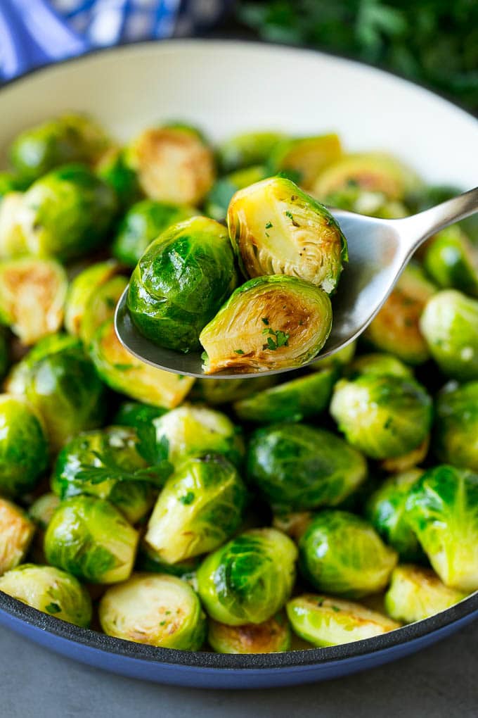 Sauteed Brussels Sprouts Recipe | Brussels Sprouts Side Dish #brusselssprouts #sprouts #veggies #sidedish #garlic #vegetarian #dinner #sraye A spoon holding up a serving of cooked brussels sprouts.