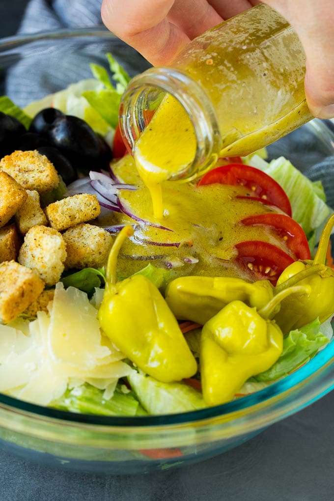 Olive Garden Salad Recipe | Italian Salad #salad #lettuce #olives #sidedish #dinner #sraye Dressing being poured over a bowl of salad.