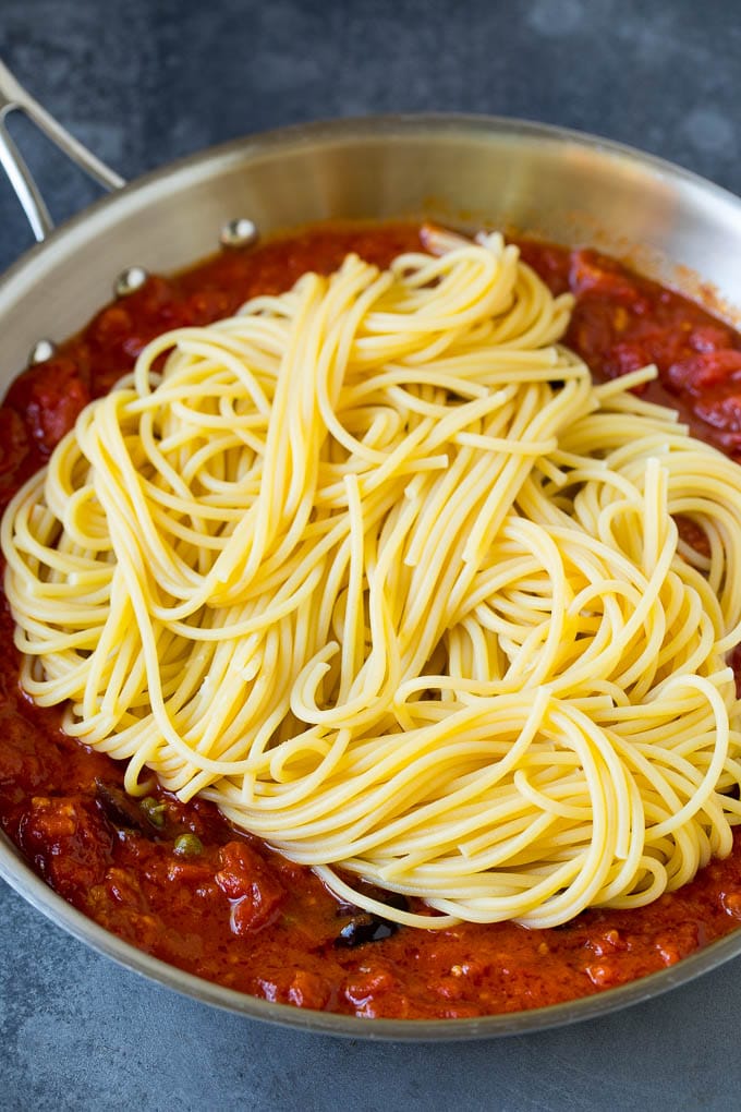 Pasta Puttanesca Recipe #pasta #tomatoes #olives #italianfood #dinner #sraye Spaghetti in a pan of tomato sauce with olives and capers.