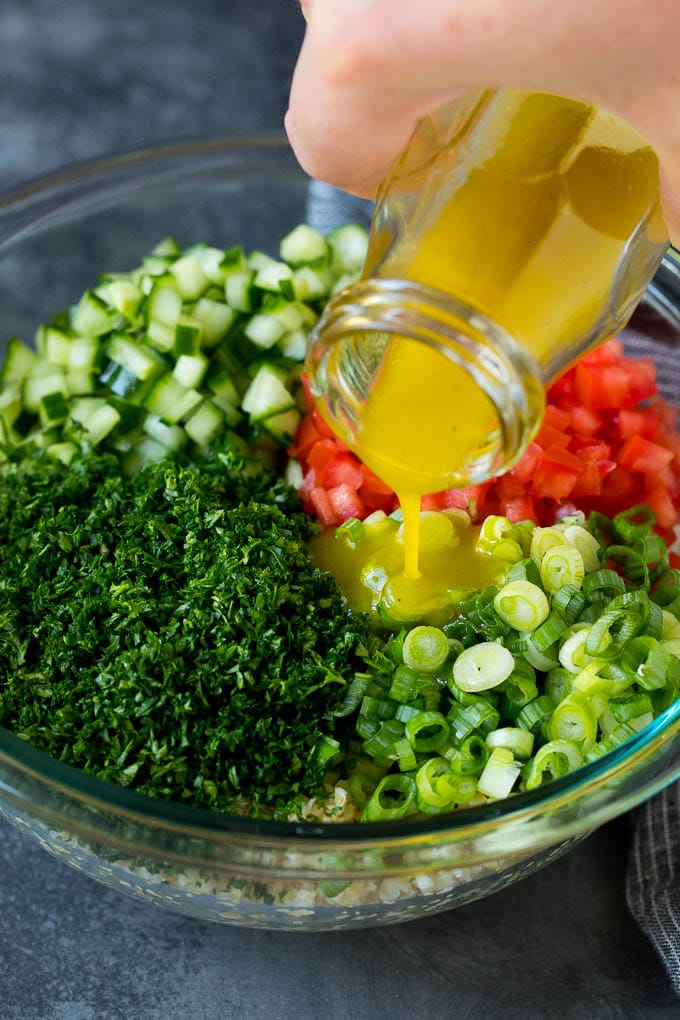 Tabbouleh Salad | Tabouli #salad #wheat #tomatoes #cucumber #healthy #sidedish #dinner #sraye Dressing being poured into a bowl of bulgur wheat salad.