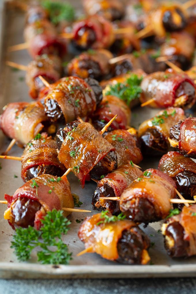 Bacon Wrapped Dates #appetizer #bacon #dates #cheese #sraye Bacon wrapped dates on a sheet pan garnished with parsley.