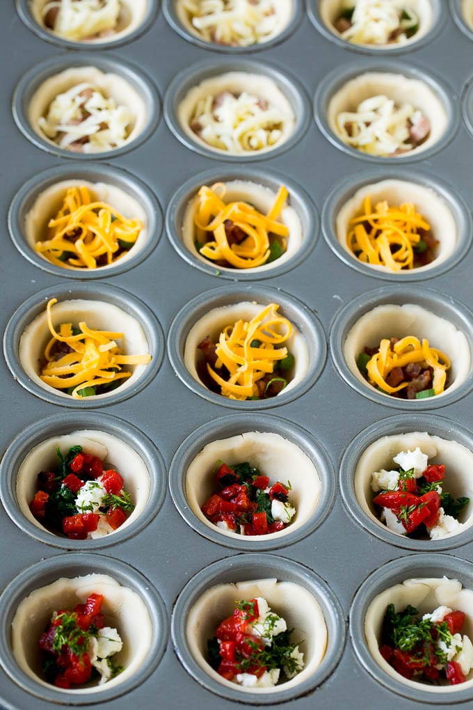 Mini Quiche Recipe #eggs #breakfast #brunch #appetizer #sraye Muffin tins filled with pie crust, vegetables, meat and shredded cheese.