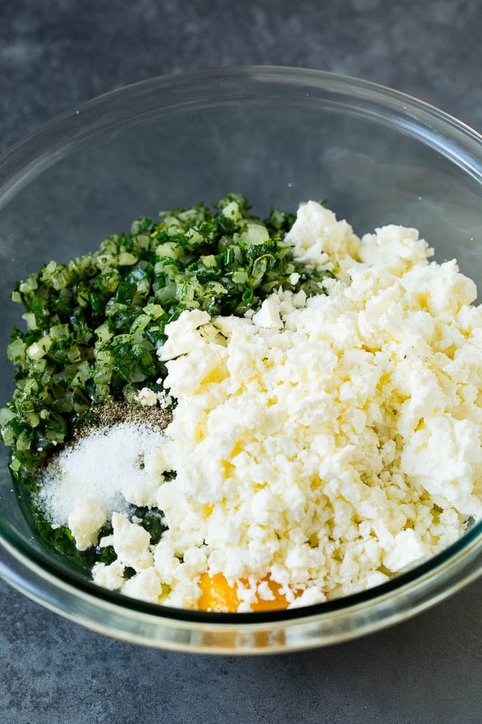 Spanakopita Recipe #appetizer #snack #spinach #cheese #sraye Spinach, onions, herbs and feta cheese in a bowl.