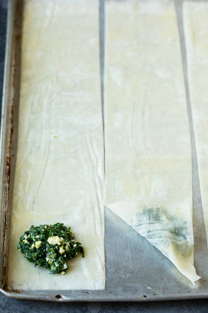 Spanakopita Recipe #appetizer #snack #spinach #cheese #sraye Strips of phyllo dough with spoonfuls of filling on top.