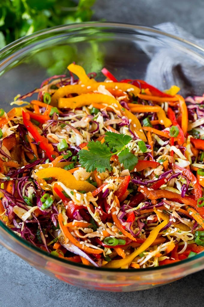 Asian Slaw Recipe #salad #slaw #sidedish #sraye A bowl of Asian slaw garnished with sesame seeds and herbs.