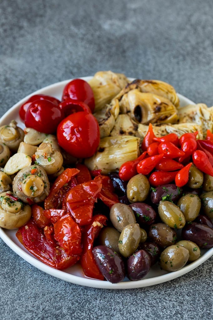 This mezze platter is filled with Mediterranean delicacies including dolmas, hummus, vegetables, pita bread and salads. #appetizer #sraye A plate of olives, peppers and grilled artichokes.