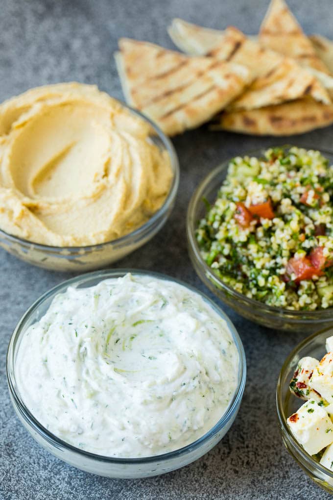 This mezze platter is filled with Mediterranean delicacies including dolmas, hummus, vegetables, pita bread and salads. #appetizer #sraye Bowls of hummus, tzatziki and tabbouleh.