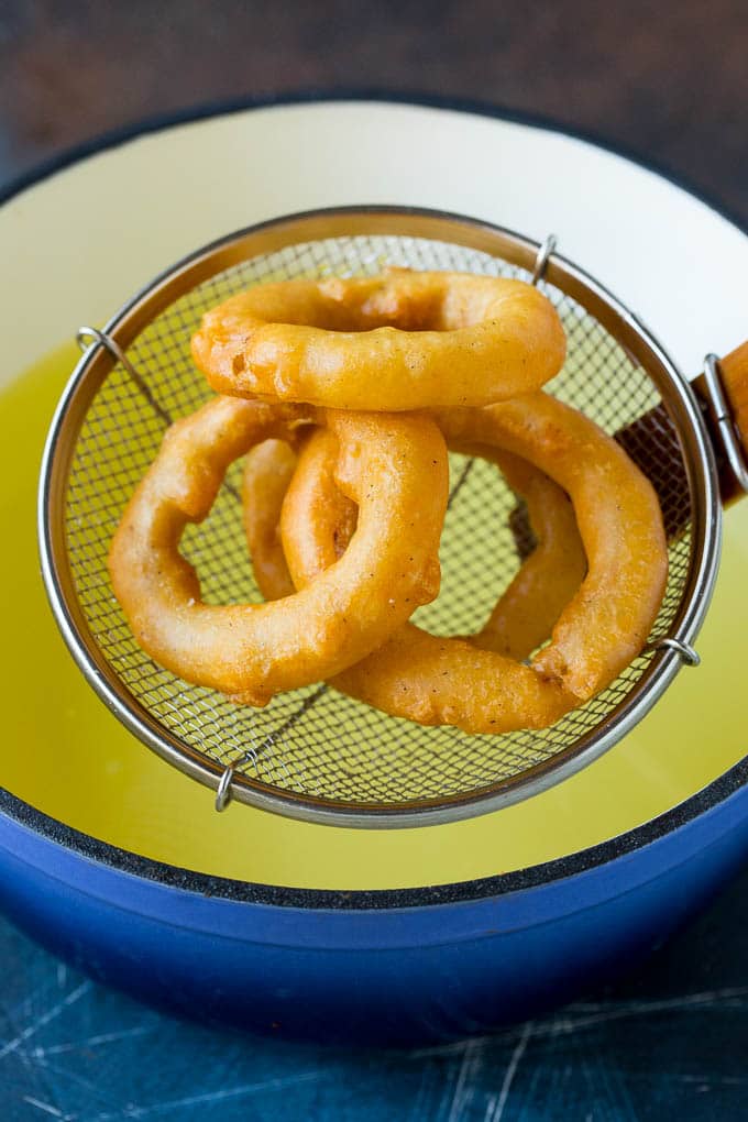 Crispy homemade onion rings that are fried in a flavorful beer batter. #onions #sraye #appetizer Fried onions coming out of a pot of oil.