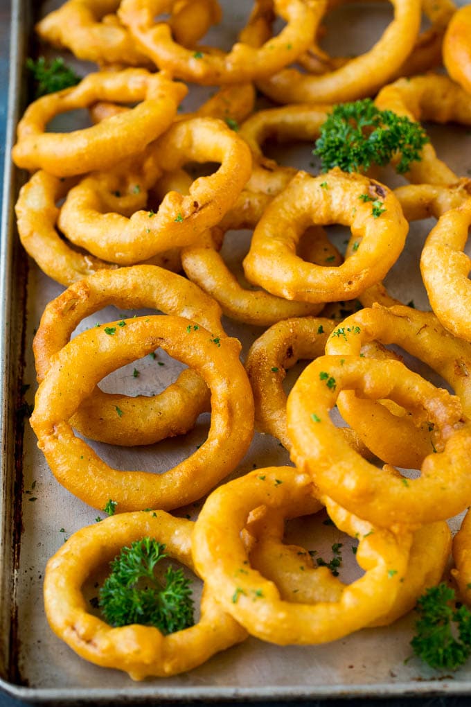 Crispy homemade onion rings that are fried in a flavorful beer batter. #onions #sraye #appetizer Beer battered onion rings on a sheet pan.