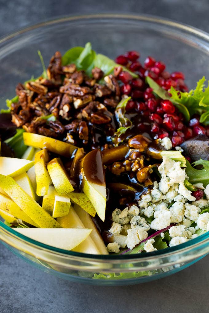 Pear Salad Recipe #salad #pears #fall #winter #dinner #sraye Balsamic dressing poured over a bowl of mixed greens, fruit and pomegranate seeds.