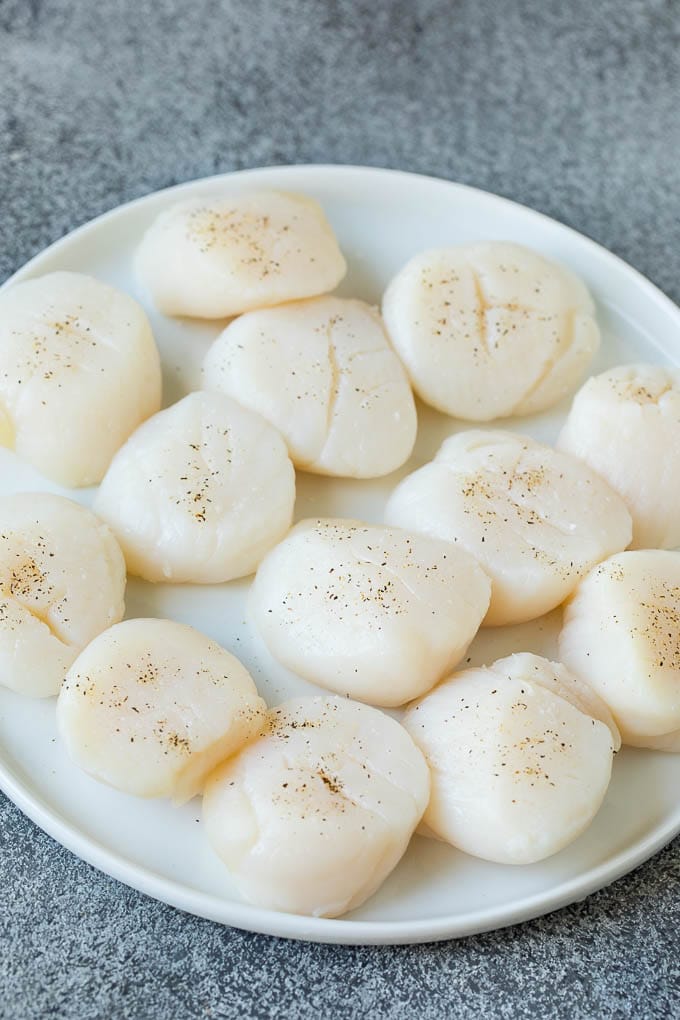Seared scallops with a garlic and herb butter sauce. An easy and elegant dinner! #seafood #dinner #sraye Raw sea scallops on a plate.