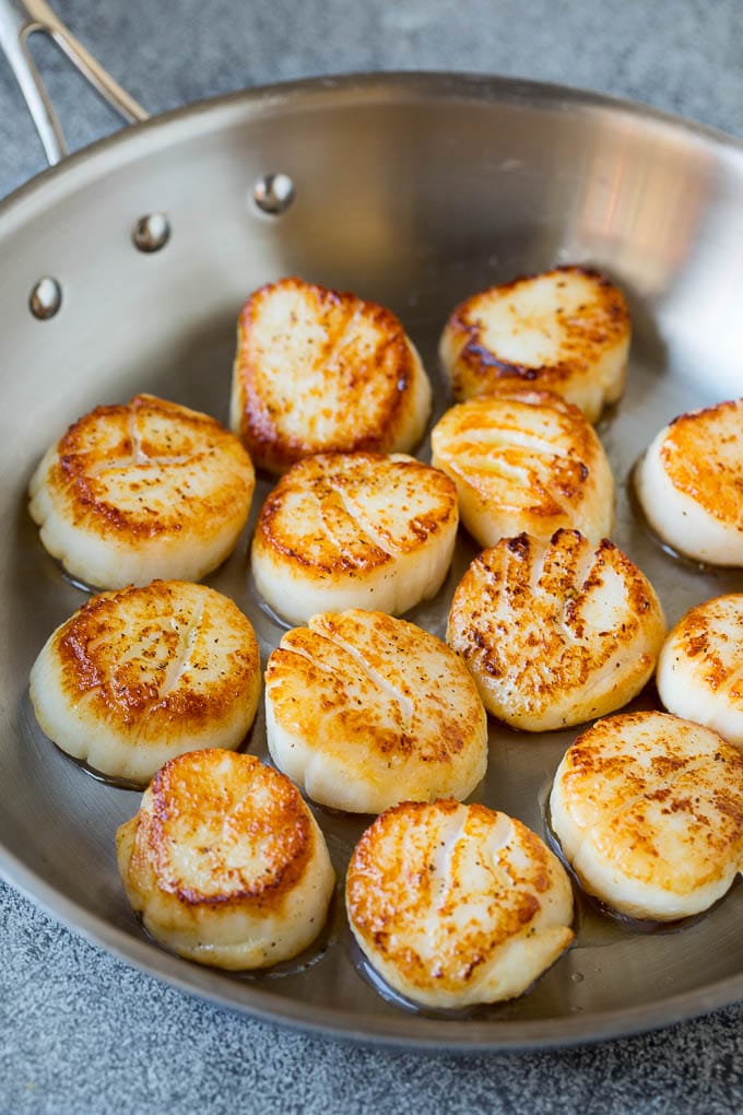 Seared scallops with a garlic and herb butter sauce. An easy and elegant dinner! #seafood #dinner #sraye Scallops cooked to golden brown in a pan.