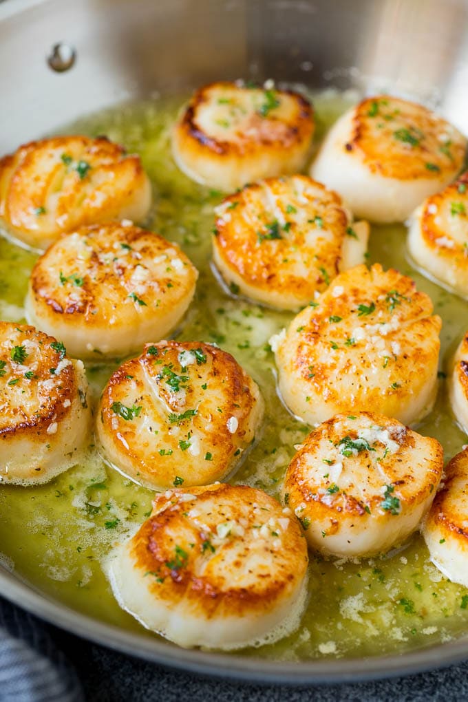 Seared scallops with a garlic and herb butter sauce. An easy and elegant dinner! #seafood #dinner #sraye A pan of scallops in garlic butter.