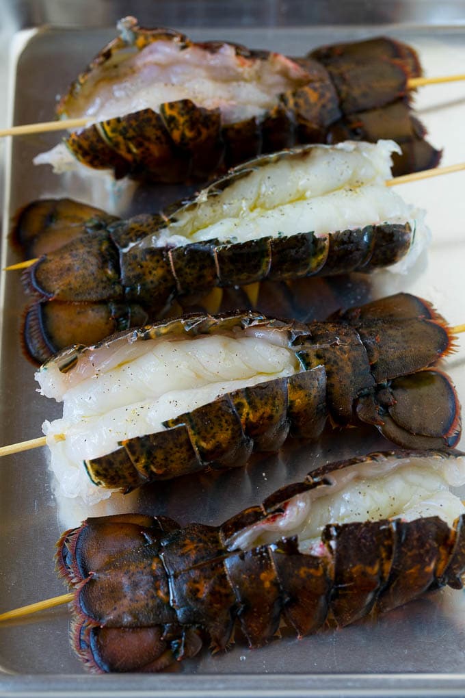 Grilled lobster tail drizzled with garlic butter is an easy and elegant dinner option. #lobster #sraye Raw lobster tails split open with skewers through them.
