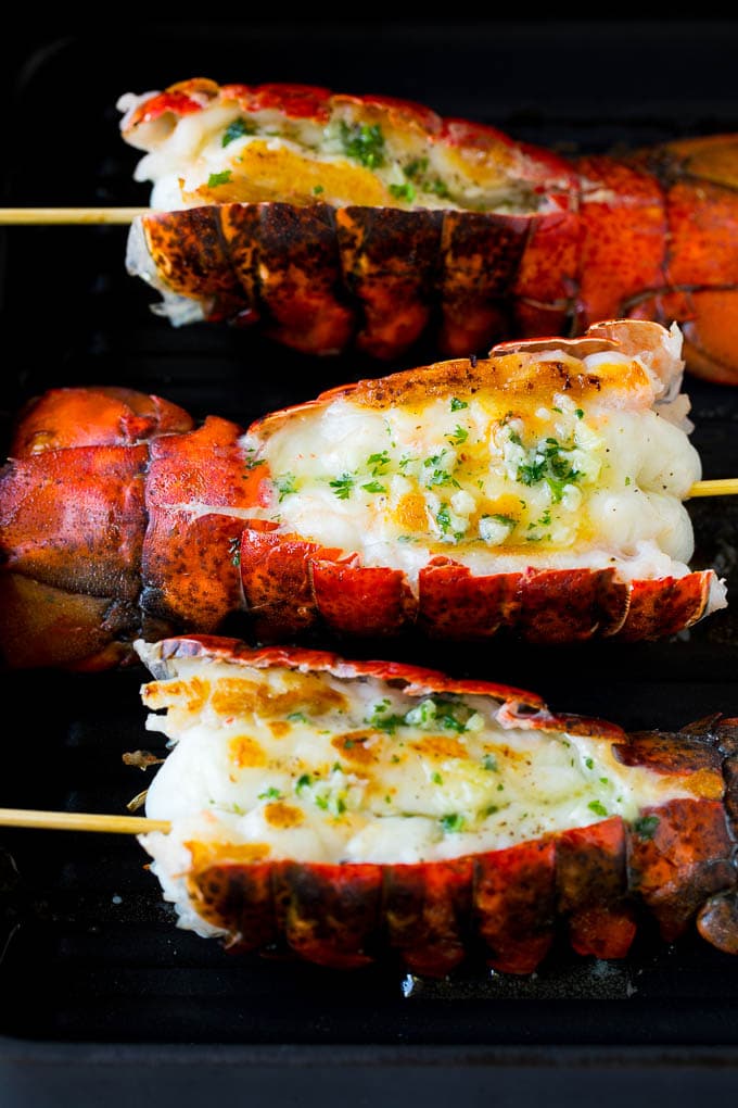 Grilled lobster tail drizzled with garlic butter is an easy and elegant dinner option. #lobster #sraye Cooked lobster tails on a grill pan, brushed with butter.