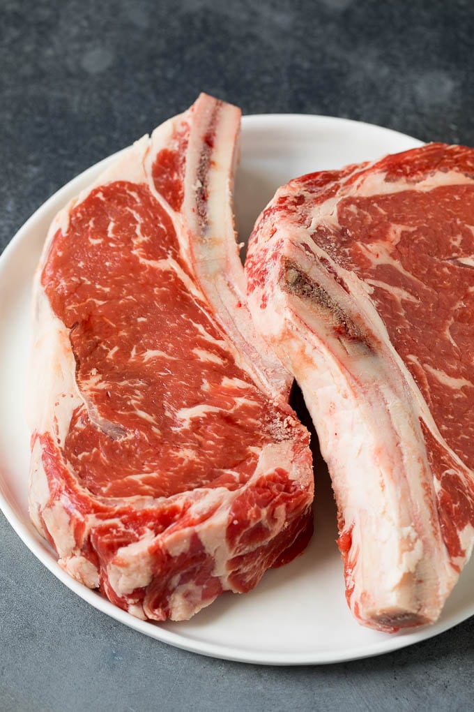 This rib eye steak recipe is tender and juicy beef seared to golden brown perfection, and topped with garlic butter and herbs. A simple steak preparation that tastes like it came from a fancy restaurant! Raw steaks on a plate.