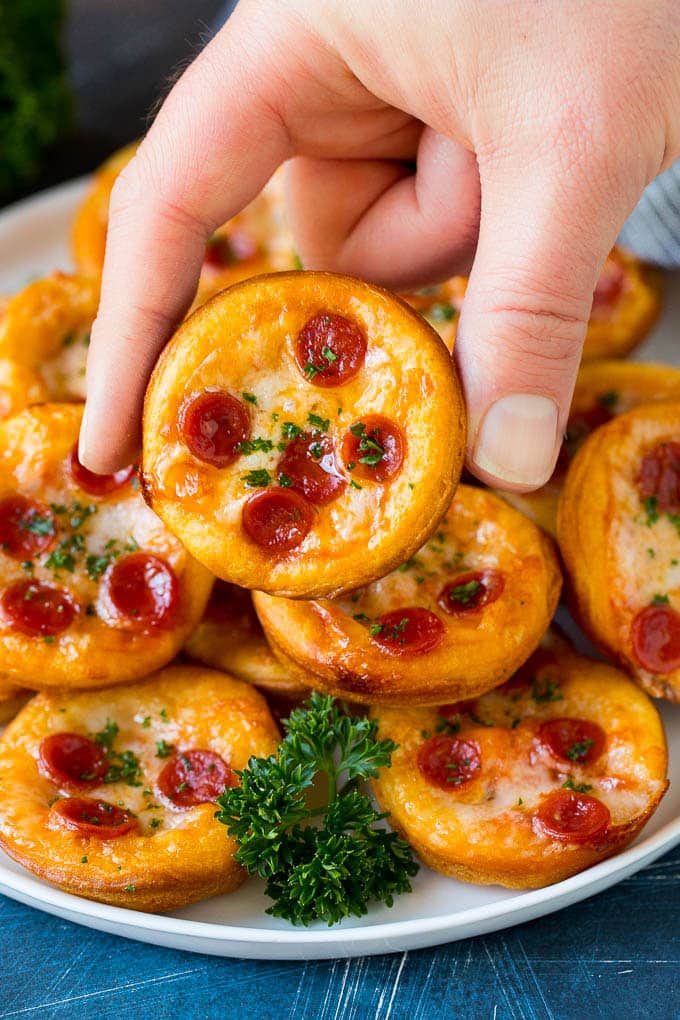 Mini pizzas topped with pepperoni are a fun and easy appetizer option. #pizza #sraye #appetizer A platter of mini pizzas with a hand reaching for one.