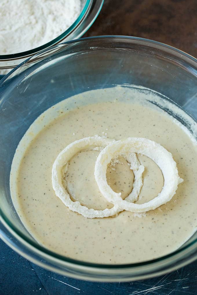 Crispy homemade onion rings that are fried in a flavorful beer batter. #onions #sraye #appetizer Floured onions in a bowl of beer batter.