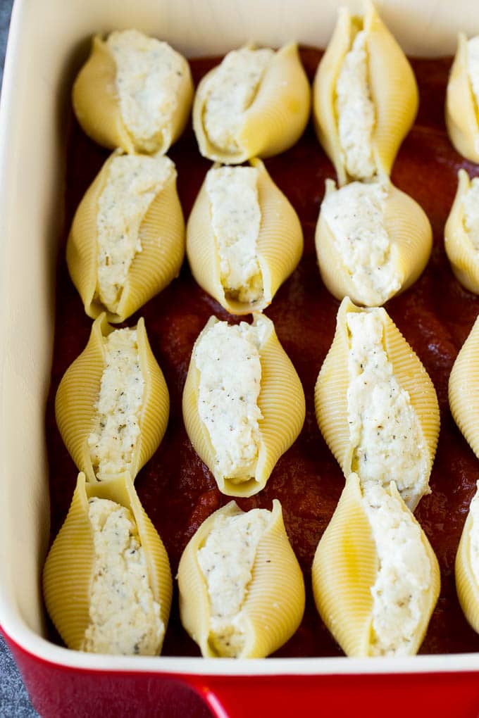 Baked stuffed shells filled with three types of cheese and topped with marinara sauce. #pasta #sraye Pasta filled with cheese on a bed of tomato sauce.