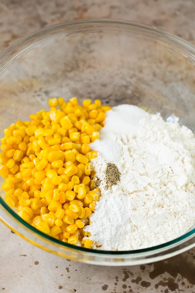 These crispy corn fritters are easy to make and are the perfect appetizer or lighter main course. #corn #sraye Flour, corn and seasonings in a mixing bowl.