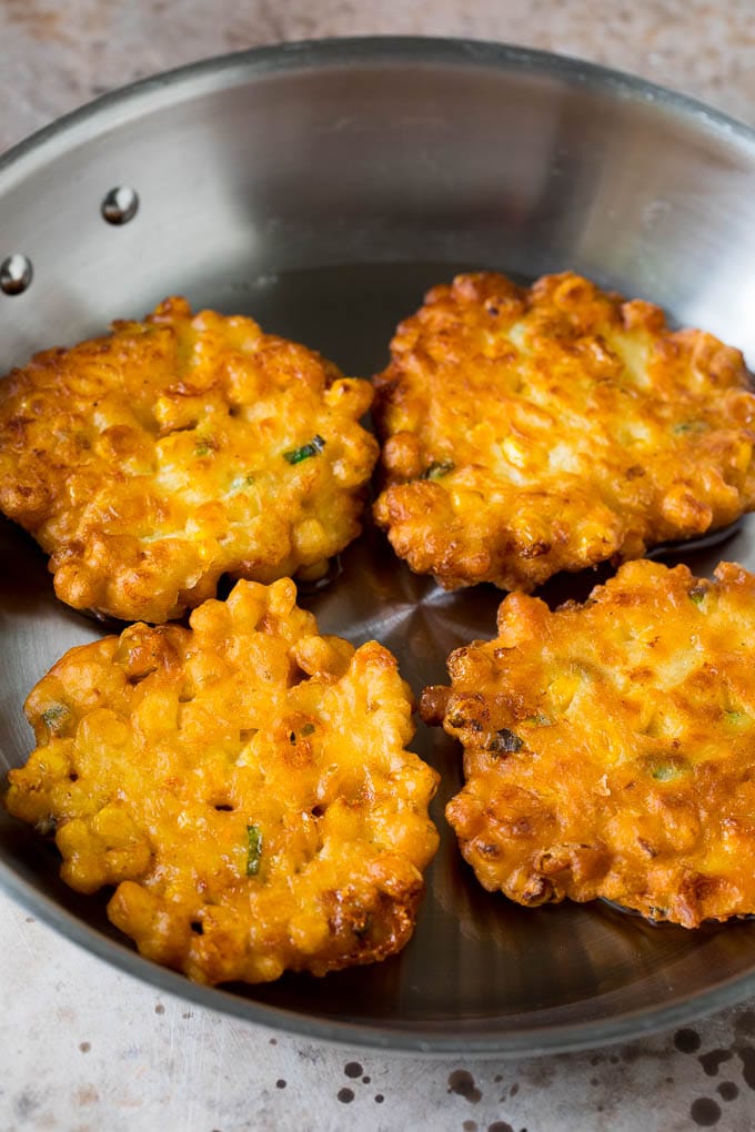 These crispy corn fritters are easy to make and are the perfect appetizer or lighter main course. #corn #sraye Corn cakes in a pan of oil.