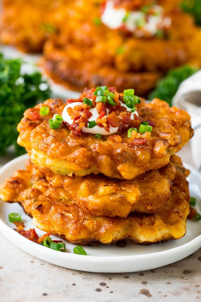 These crispy corn fritters are easy to make and are the perfect appetizer or lighter main course. #corn #sraye A stack of corn fritters topped with bacon, sour cream and green onions.