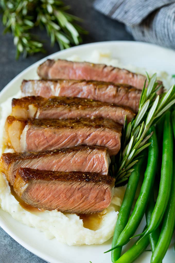 This rib eye steak recipe is tender and juicy beef seared to golden brown perfection, and topped with garlic butter and herbs. A simple steak preparation that tastes like it came from a fancy restaurant! Sliced rib eye steak served with mashed potatoes and green beans.