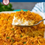 A serving spoon of funeral potatoes served out of a baking dish.