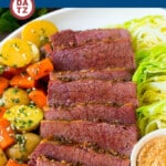 A plate with corned beef and cabbage with potatoes carrots and a little mustard.