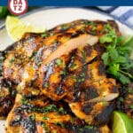 A plate of grilled chicken thighs garnished with cilantro leaves and lime wedges.